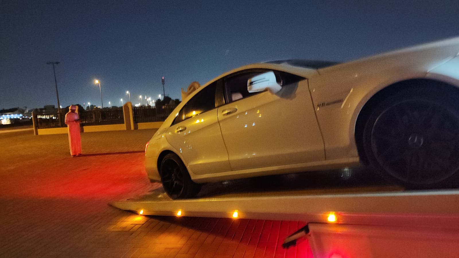 White performance car being winched onto a flatbed at night in Dubai