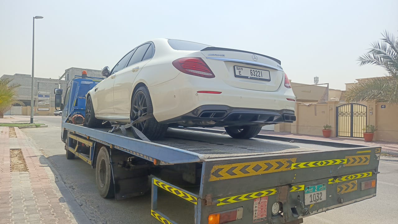White luxury sedan on blue flatbed tow truck in a Dubai neighborhood