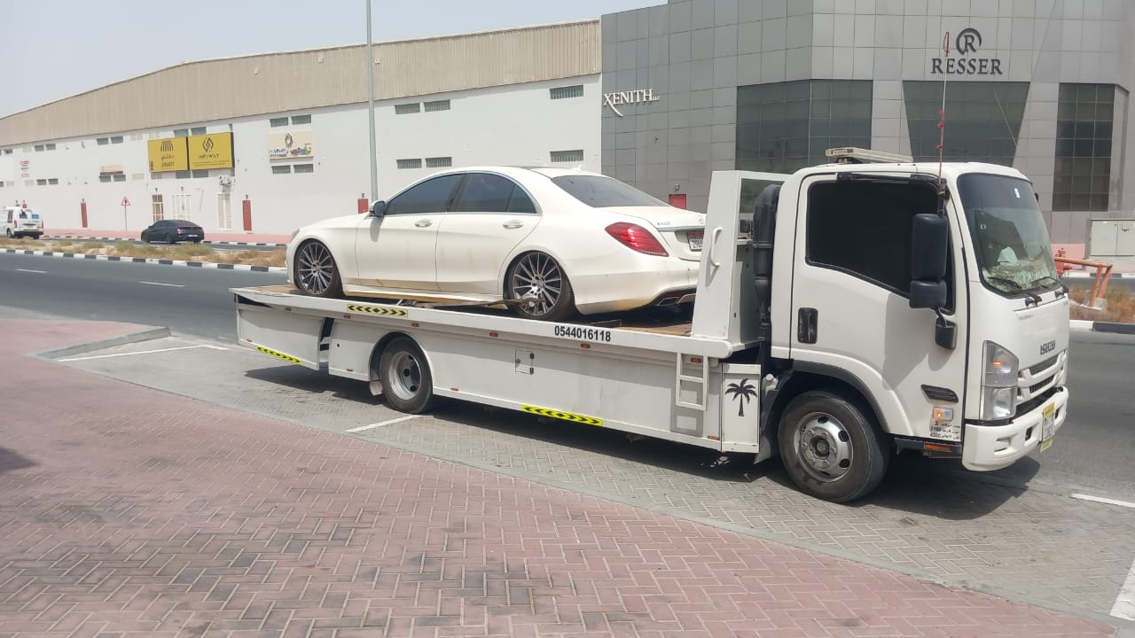 White luxury car on a modern flatbed tow truck near warehouses